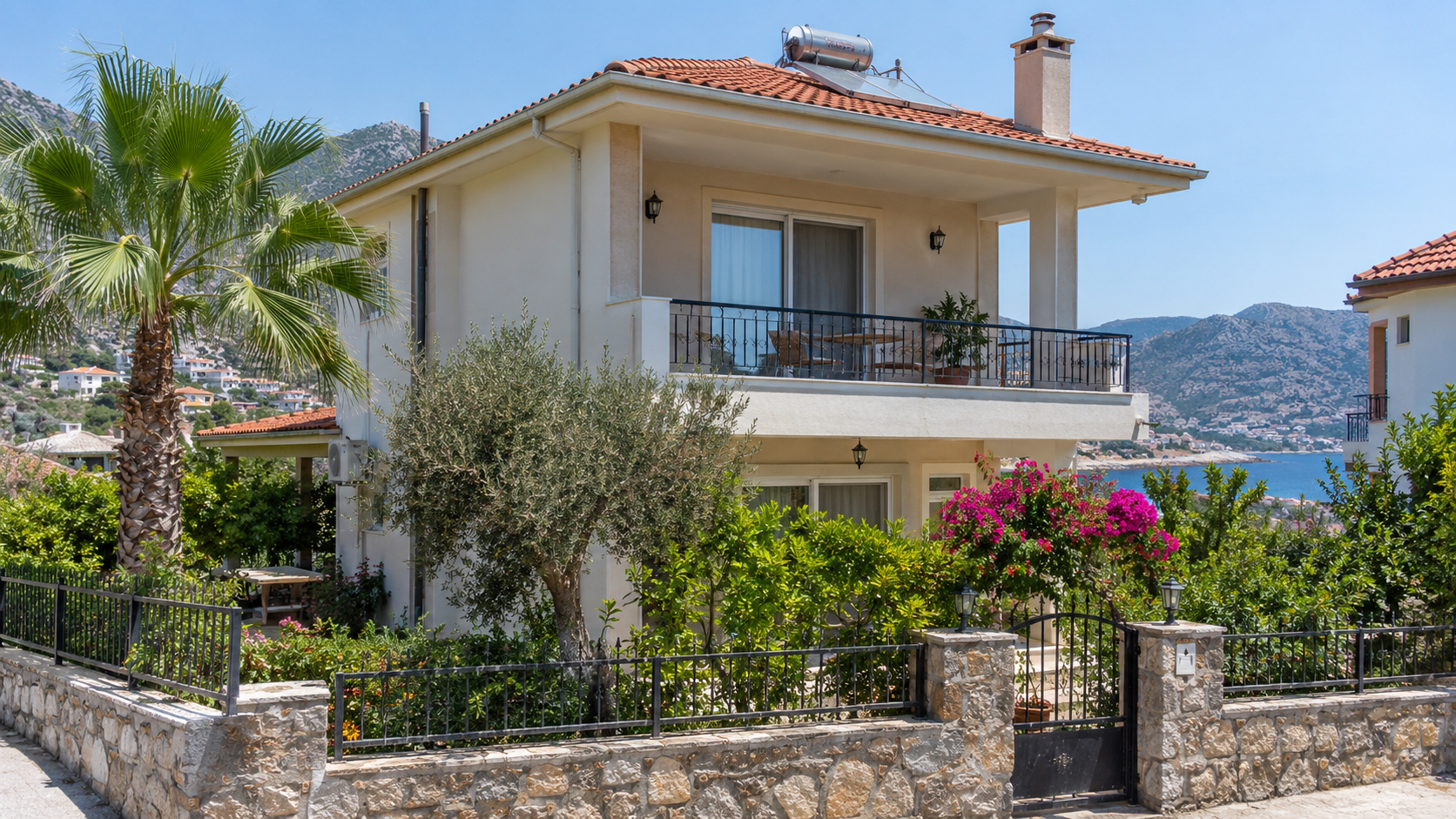 Taş duvarlı bahçesinde palmiye, zeytin ağacı ve begonviller bulunan, balkonlu iki katlı deniz manzaralı bir villa